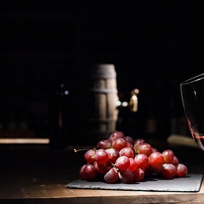 Woman holds glass of wine before bunch of grape lying on black p