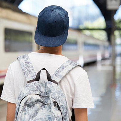 Back view of teenage school boy wearing white T-shirt and cap with a backpack on his back walking home from school. Urban background with copy space for your advertising content. Selective focus Back view of teenage school boy wearing white T-shirt and cap with a backpack on his back walking home from school. Urban background with copy space for your advertising content. Selective focus