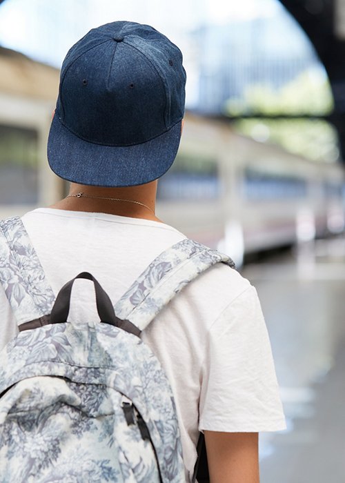 Back view of teenage school boy wearing white T-shirt and cap with a backpack on his back walking home from school. Urban background with copy space for your advertising content. Selective focus Back view of teenage school boy wearing white T-shirt and cap with a backpack on his back walking home from school. Urban background with copy space for your advertising content. Selective focus
