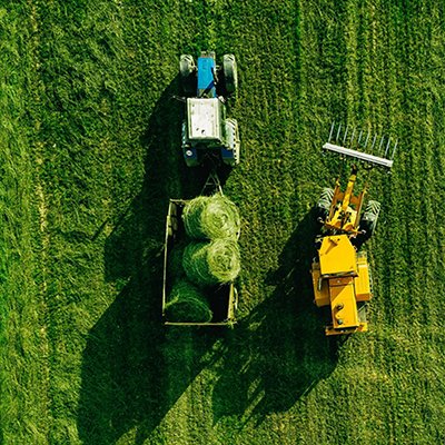 Aerial view of harvest field with tractor moving hay bale 