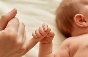 Faceless mother with naked baby, infant holding mommy's finger, mum spending time with her tiny child on light background.