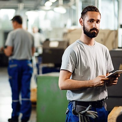 Young engineer with touchpad operating a CNC machine and looking at camera. Young engineer with touchpad operating a CNC machine and looking at camera.