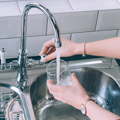 Woman filling the glass with water from the steel faucet in the kitchen Woman filling the glass with water from the steel faucet in the kitchen