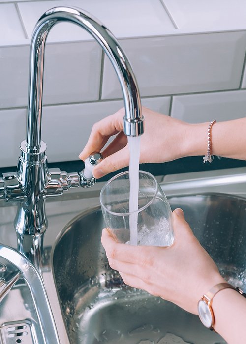 Woman filling the glass with water from the steel faucet in the kitchen Woman filling the glass with water from the steel faucet in the kitchen