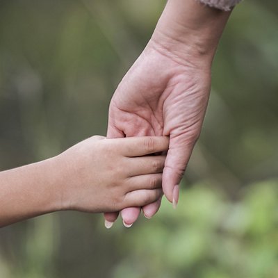 Close up of happy mum and son holding hand in a park. Family concept.