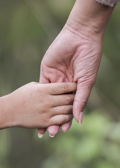 Close up of happy mum and son holding hand in a park. Family concept.