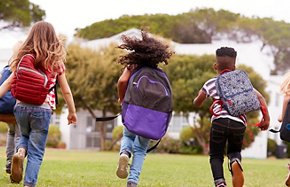 Rear View Of  Elementary School Pupils Running Across Field At Break Time