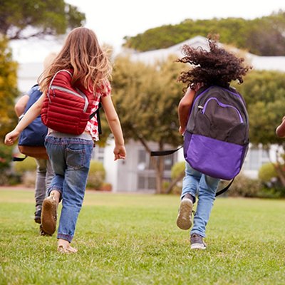 Rear View Of  Elementary School Pupils Running Across Field At Break Time