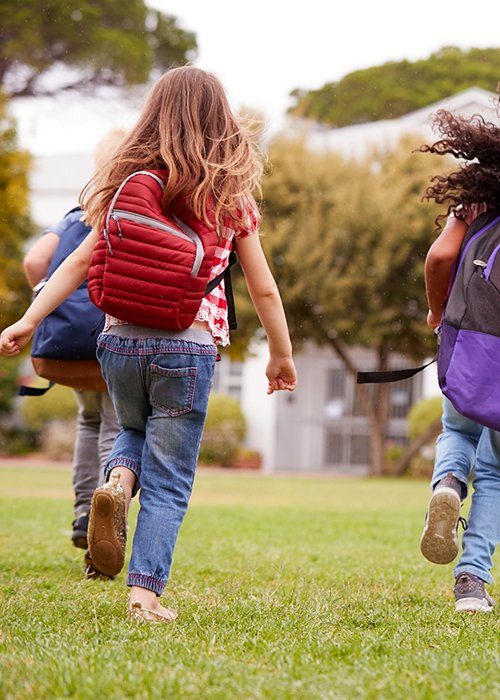 Rear View Of  Elementary School Pupils Running Across Field At Break Time