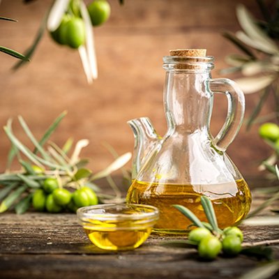 Glass bottle of olive oil with fresh green olives and olive branches on rustic table