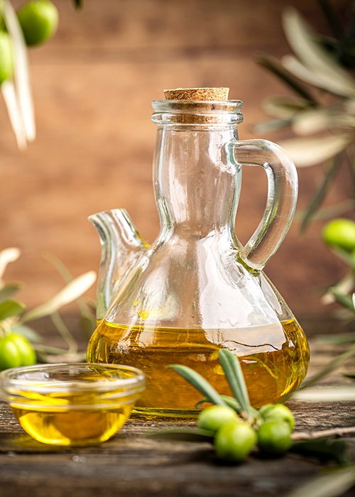 Glass bottle of olive oil with fresh green olives and olive branches on rustic table