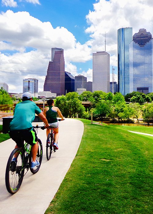 Riding Bikes on Paved Trail in Houston Park (view of river and skyline of downtown Houston) - Houston, Texas, USA