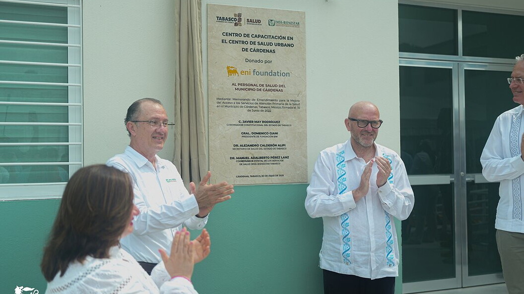 Two men and a woman applaud in front of a wall with plaques and inscriptions