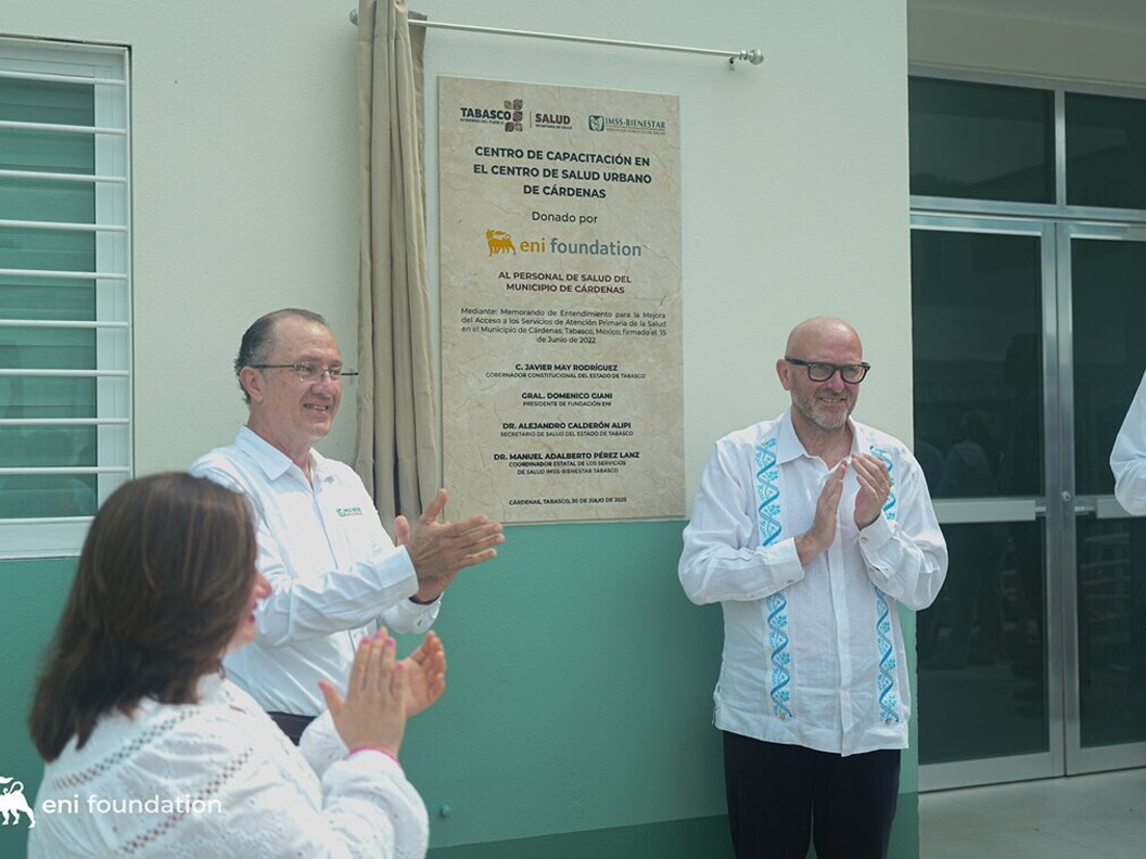 Two men and a woman applaud in front of a wall with plaques and inscriptions