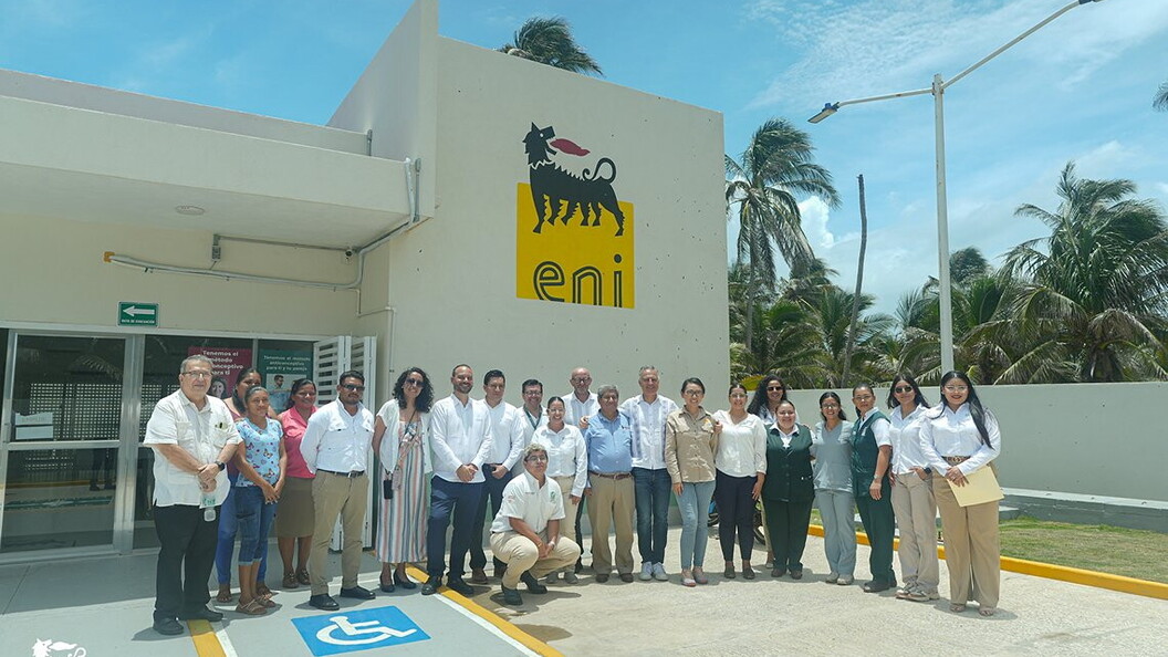 A group of people pose in front of the entrance to a building bearing the Eni logo