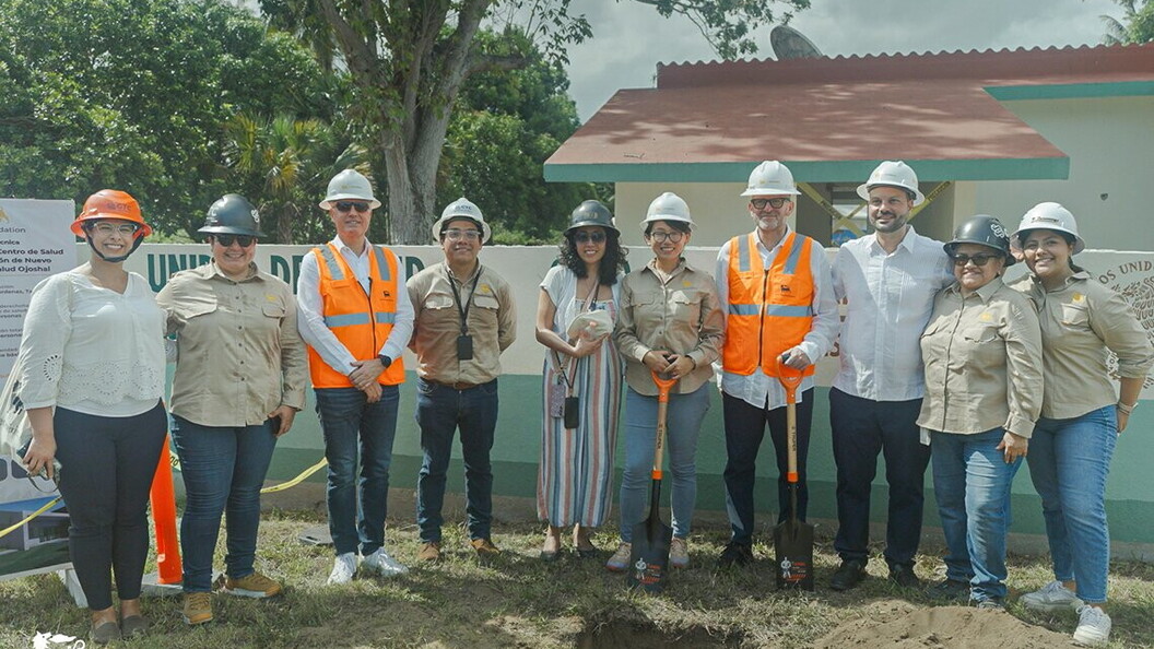 A group of people wearing helmets and orange jackets pose in front of a building