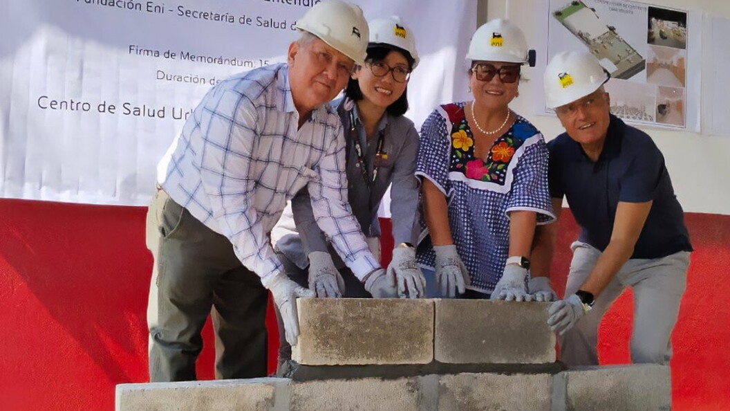 Four people wearing safety helmets position concrete blocks during a ceremony