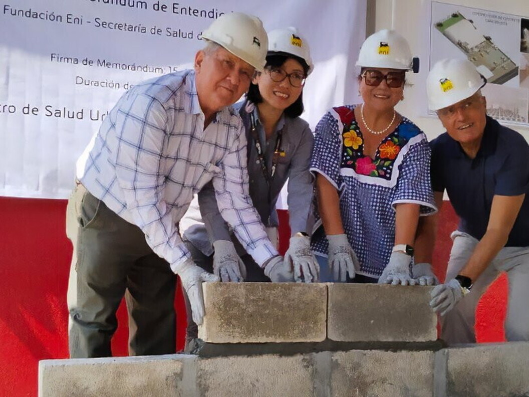 Four people wearing safety helmets position concrete blocks during a ceremony