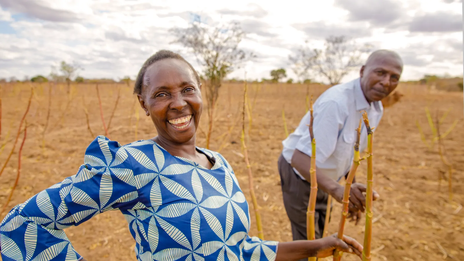 A smiling woman and man work the land with farming tools.