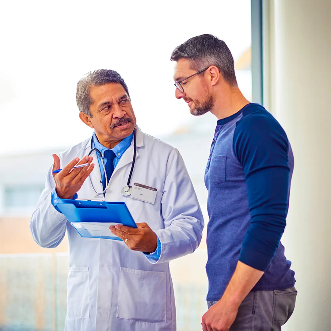 A doctor in a white coat talking to a man in front of a window.