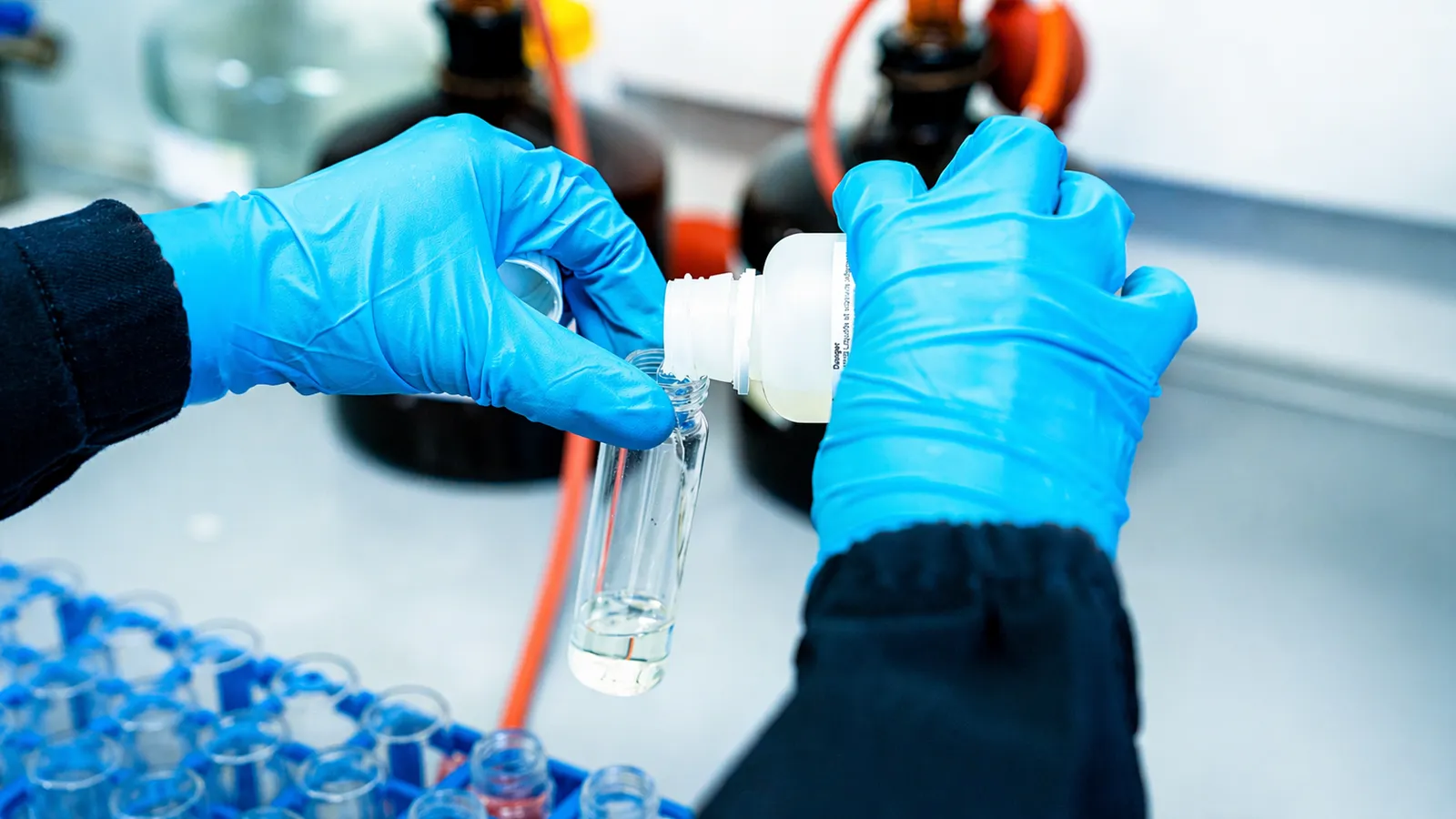 Close-up of hands with blue gloves handling a vial in a scientific laboratory setting.