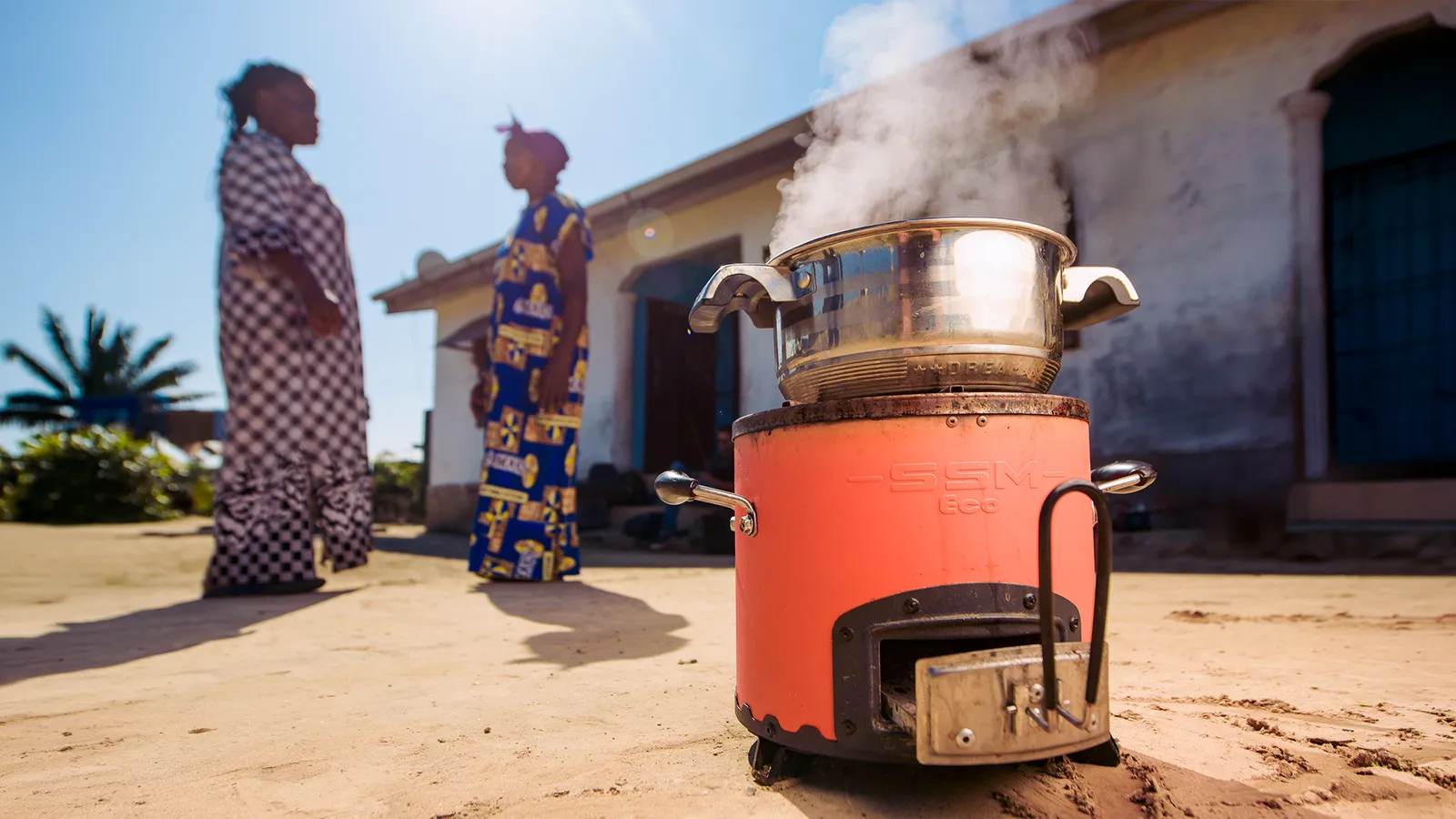 Close-up of an improved cookstove with two women in African clothing in the background.
